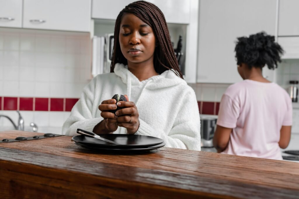 African American woman preparing food at a kitchen counter, wearing a white hoodie.